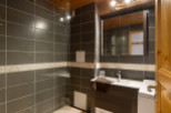 This modern bathroom boasts dark gray tiled walls, a glass shower enclosure, and a stylish dark wood vanity with a white sink.