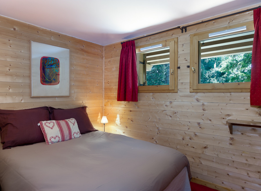 Cozy wooden cabin room with comfortable double bed and red curtains.