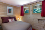 Cozy wooden cabin room with comfortable double bed and red curtains.