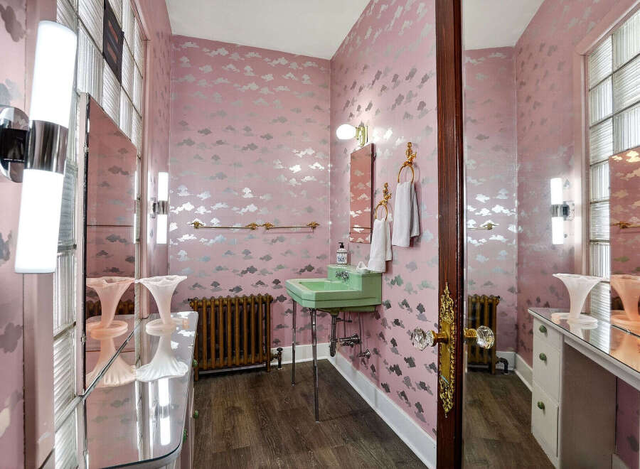 Step into a whimsical bathroom retreat! This space features a unique cloud-patterned wallpaper, a vintage green sink, and elegant fixtures.