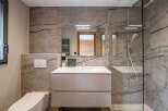 This modern bathroom showcases a sleek design with its marble-effect tiled walls and a frameless glass shower enclosure.