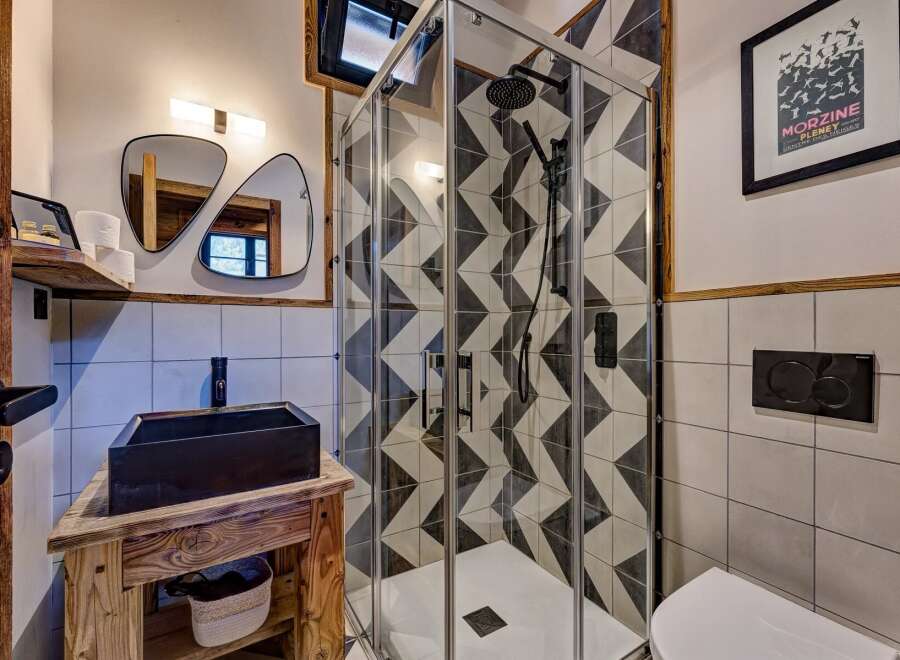 This modern bathroom boasts a stylish design with a geometric tiled shower and a sleek black sink.