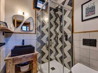 This modern bathroom boasts a stylish design with a geometric tiled shower and a sleek black sink.