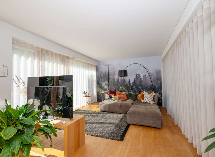Experience modern living in this stylish property, featuring a spacious living room with a cozy sectional sofa and a stunning forest-themed accent wall.