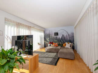 Experience modern living in this stylish property, featuring a spacious living room with a cozy sectional sofa and a stunning forest-themed accent wall.