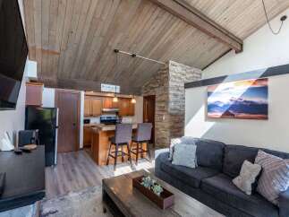 This stunning property boasts a cozy living space with a rustic charm, featuring a beautiful wooden ceiling and a stone accent wall.