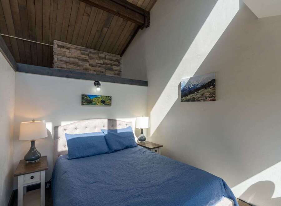 Discover the charm of this cozy bedroom featuring a unique architectural design with exposed wooden beams and a stone accent wall.
