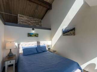 Discover the charm of this cozy bedroom featuring a unique architectural design with exposed wooden beams and a stone accent wall.