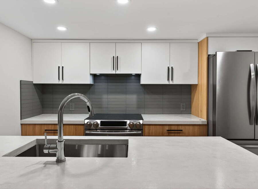 This modern kitchen boasts sleek white cabinetry, complemented by warm wood accents and a stylish gray backsplash.