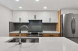 This modern kitchen boasts sleek white cabinetry, complemented by warm wood accents and a stylish gray backsplash.