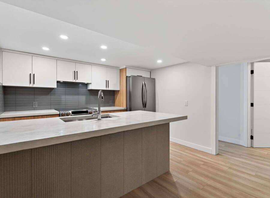 This modern kitchen boasts sleek white cabinetry, a stylish gray backsplash, and a spacious island with a concrete countertop.
