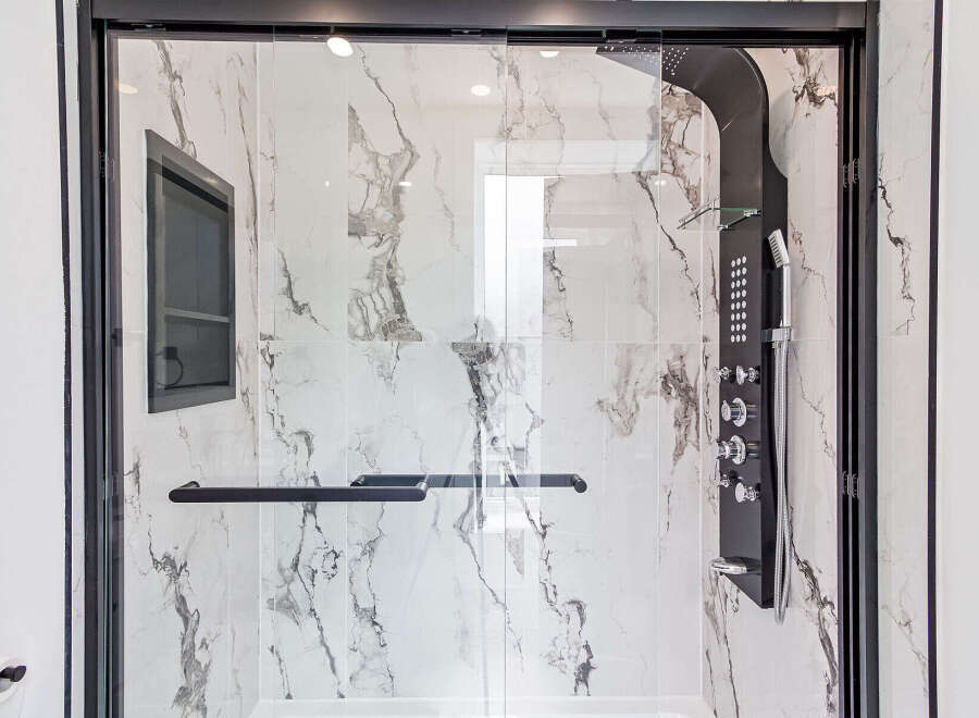Step into luxury with this stunning shower featuring a sleek black shower panel and elegant marble-look tiles.