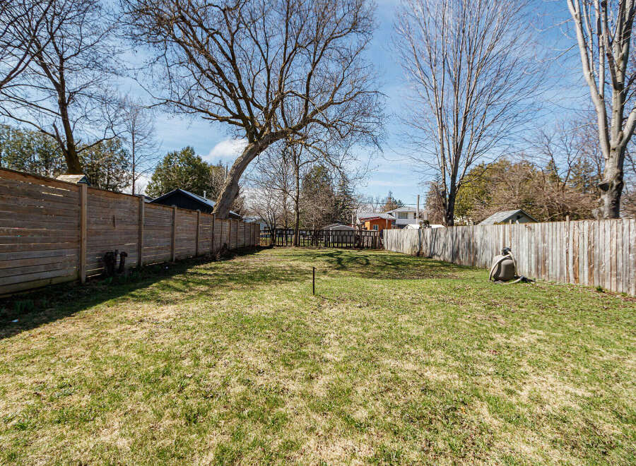 This spacious backyard offers a serene escape with its lush green lawn and wooden fence.