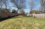 This spacious backyard offers a serene escape with its lush green lawn and wooden fence.