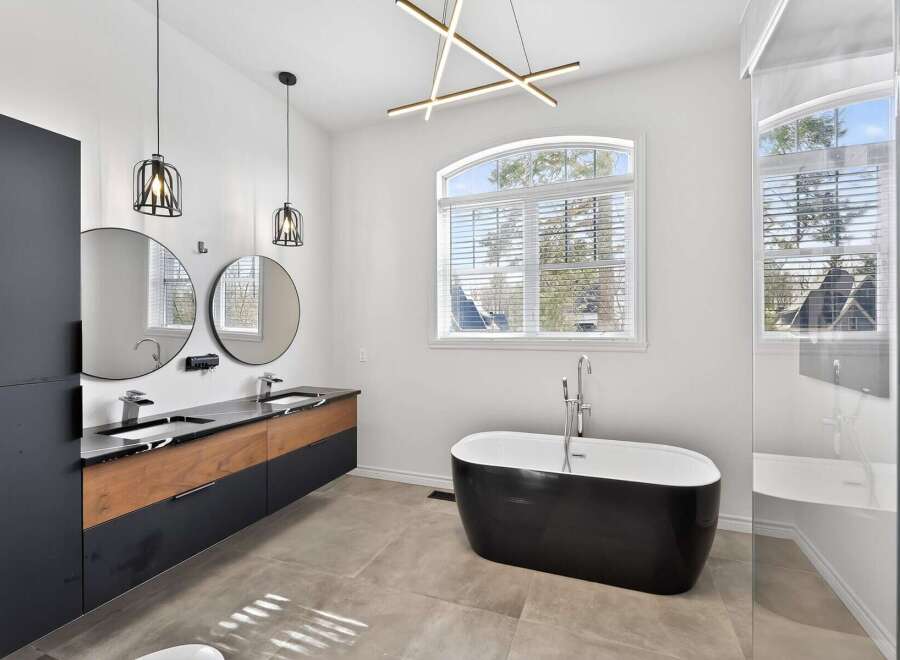 This luxurious bathroom boasts a modern design with sleek black and wood cabinetry, complemented by round mirrors and stylish pendant lighting.