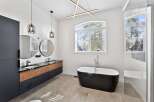 This luxurious bathroom boasts a modern design with sleek black and wood cabinetry, complemented by round mirrors and stylish pendant lighting.