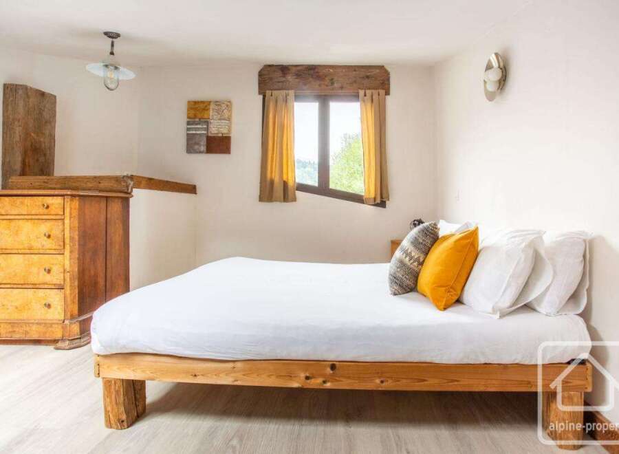 Discover the charm of this cozy bedroom, featuring a rustic wooden bed frame and a bright, airy atmosphere.