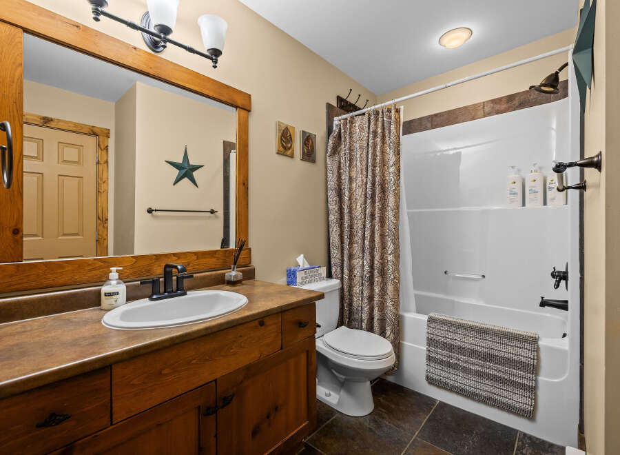 This charming bathroom features a rustic wooden vanity with ample storage, complemented by a sleek white sink and modern black faucet.