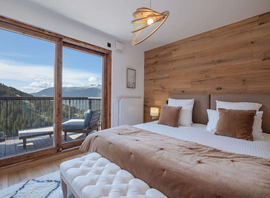 Experience breathtaking mountain views from this luxurious bedroom, featuring a spacious king-size bed with plush bedding and a cozy throw.