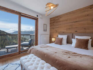 Experience breathtaking mountain views from this luxurious bedroom, featuring a spacious king-size bed with plush bedding and a cozy throw.