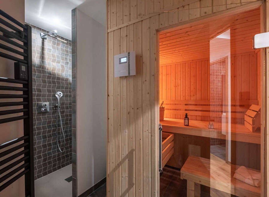 Experience ultimate relaxation in this modern spa area, featuring a sleek shower with geometric tilework and a luxurious, glass-enclosed sauna.