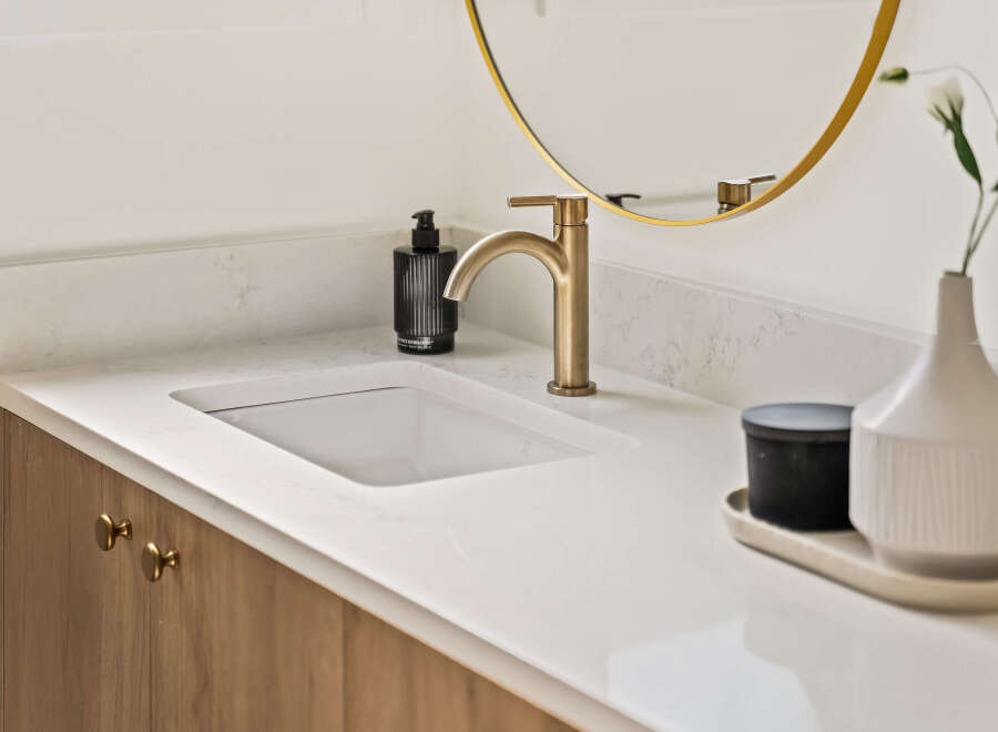 This stunning bathroom features a modern design with a sleek white countertop and a stylish gold faucet.