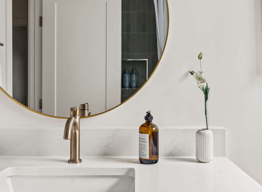 This modern bathroom boasts a sleek design with a round gold-framed mirror, a stylish faucet, and a pristine white countertop.
