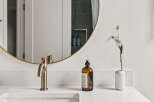 This modern bathroom boasts a sleek design with a round gold-framed mirror, a stylish faucet, and a pristine white countertop.