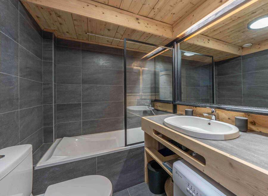 This modern bathroom features a sleek design with gray tiled walls and a wooden ceiling, creating a warm and inviting atmosphere.