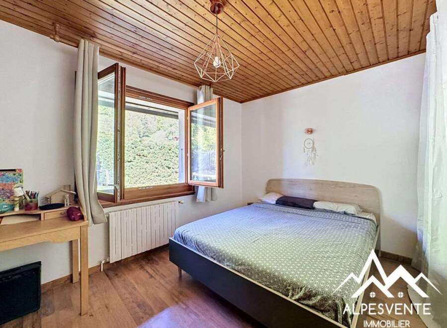 Discover this charming bedroom featuring a cozy wooden ceiling and a bright window overlooking lush greenery.