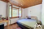 Discover this charming bedroom featuring a cozy wooden ceiling and a bright window overlooking lush greenery.