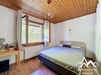 Discover this charming bedroom featuring a cozy wooden ceiling and a bright window overlooking lush greenery.