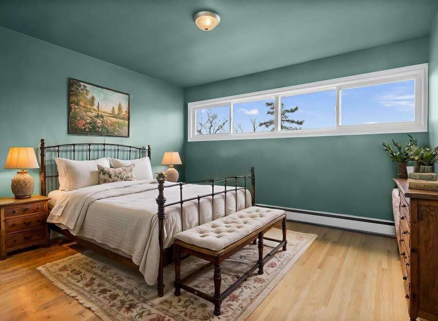 This charming bedroom boasts a serene ambiance with its calming teal walls and natural wood flooring.