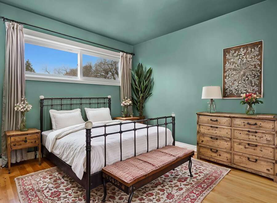 This inviting bedroom boasts a serene ambiance with its calming teal walls and natural light streaming through the window.