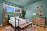 This inviting bedroom boasts a serene ambiance with its calming teal walls and natural light streaming through the window.