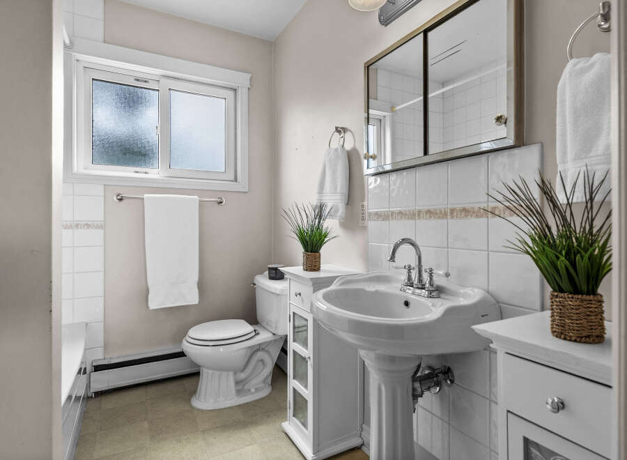 This charming bathroom features a classic pedestal sink, a pristine white toilet, and a bright window.