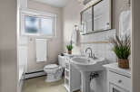 This charming bathroom features a classic pedestal sink, a pristine white toilet, and a bright window.