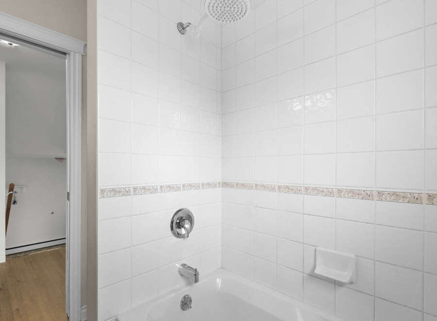 This pristine bathroom features a clean, modern design with white tile walls and a matching bathtub.