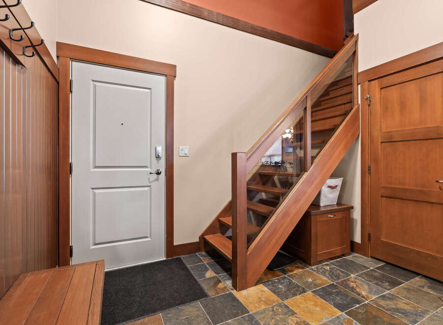 Step into this inviting entryway, showcasing a stunning staircase with glass panels and rich wooden accents.