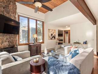 This stunning living room boasts a cozy ambiance with a stone fireplace and a beautiful wooden ceiling.