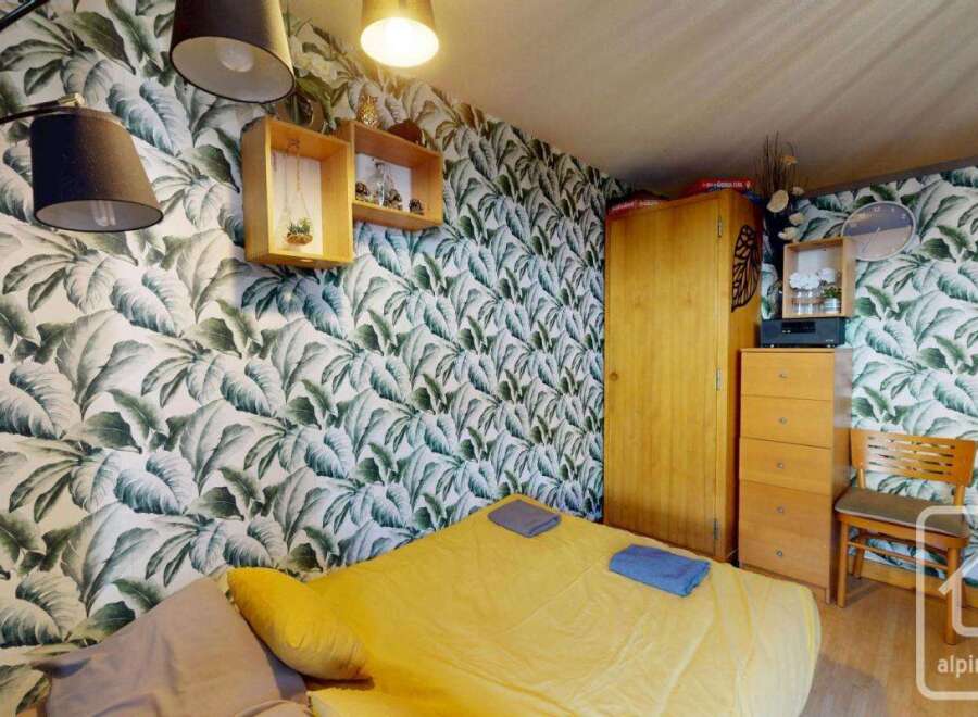 This cozy bedroom features a vibrant tropical leaf wallpaper, creating a refreshing and inviting atmosphere.