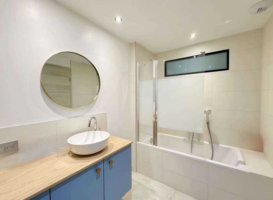 This modern bathroom boasts a sleek design with a round mirror, a stylish sink, and a bathtub.