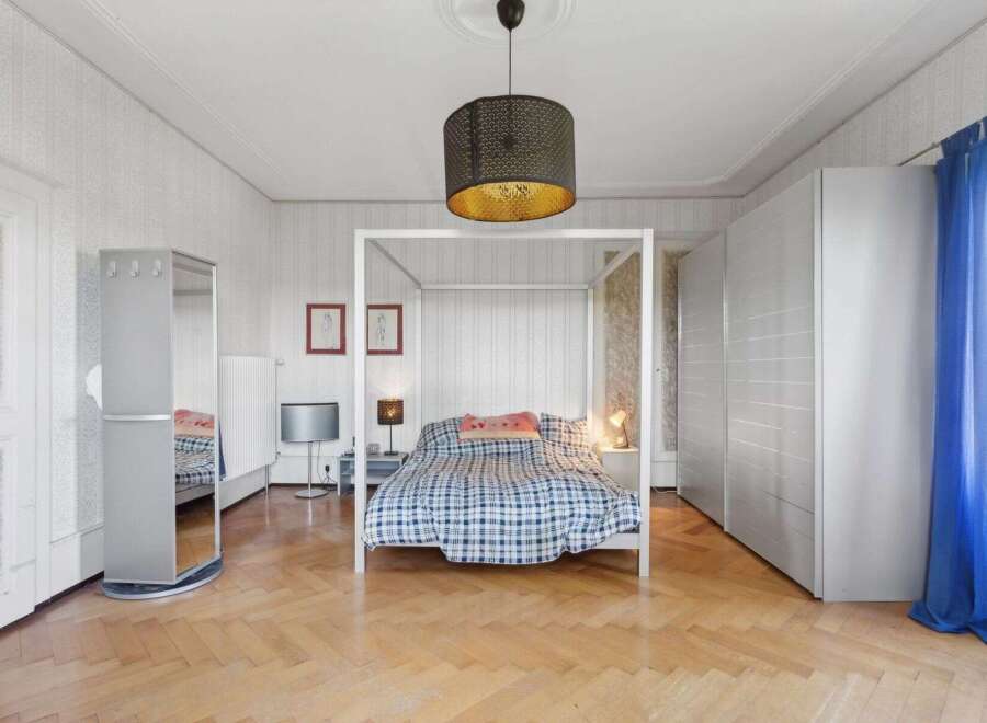This spacious bedroom features a stylish four-poster bed with a cozy plaid comforter, creating a comfortable and inviting atmosphere.