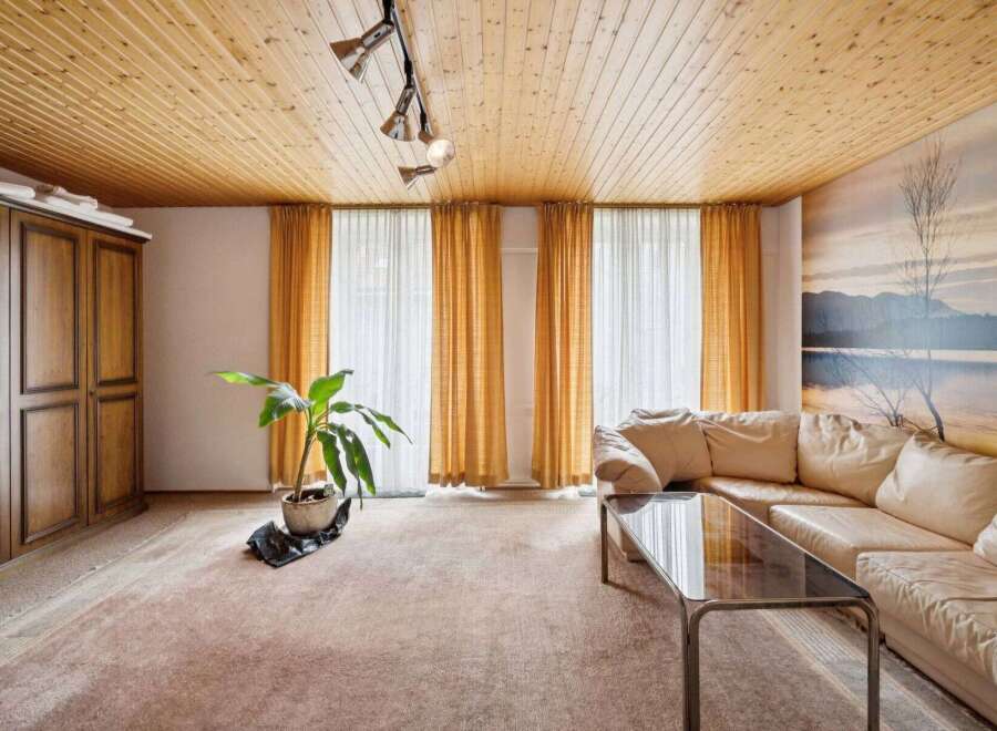 Step into this inviting living space, featuring a warm, wooden ceiling and ample natural light streaming through the large windows.