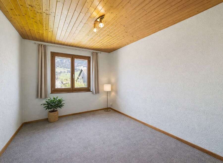 Experience serene living in this charming room featuring a warm wooden ceiling and a large window with picturesque mountain views.