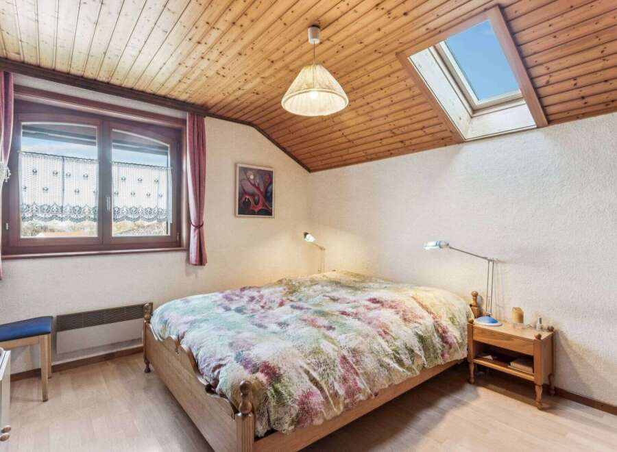 This charming bedroom features a cozy wooden ceiling and a skylight, creating a bright and airy atmosphere.