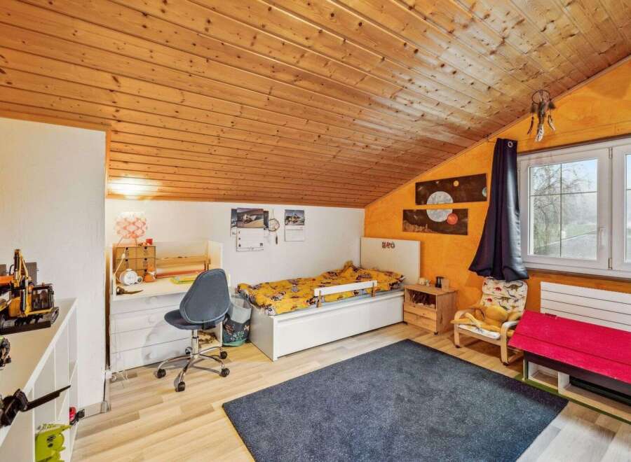 This charming bedroom features a cozy, sloped wooden ceiling and a vibrant orange accent wall.