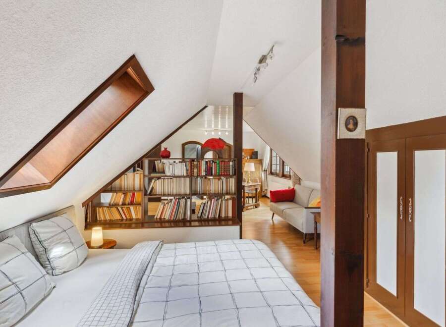 Discover the charm of this unique attic bedroom, featuring a cozy bed and a built-in bookshelf.