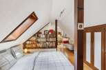 Discover the charm of this unique attic bedroom, featuring a cozy bed and a built-in bookshelf.