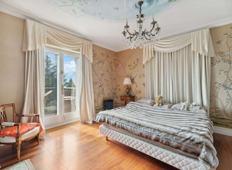 Step into luxury with this exquisite bedroom, featuring a stunning chandelier and elegant curtains.